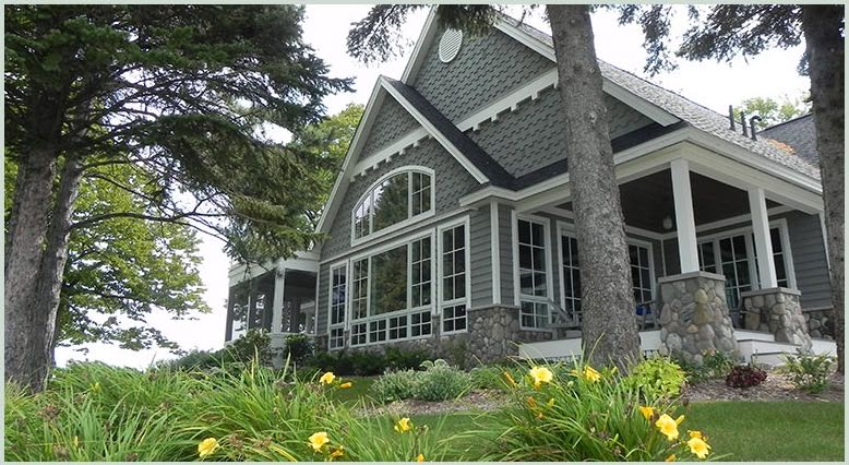 Gray lake home with a wraparound screened porch among tall trees